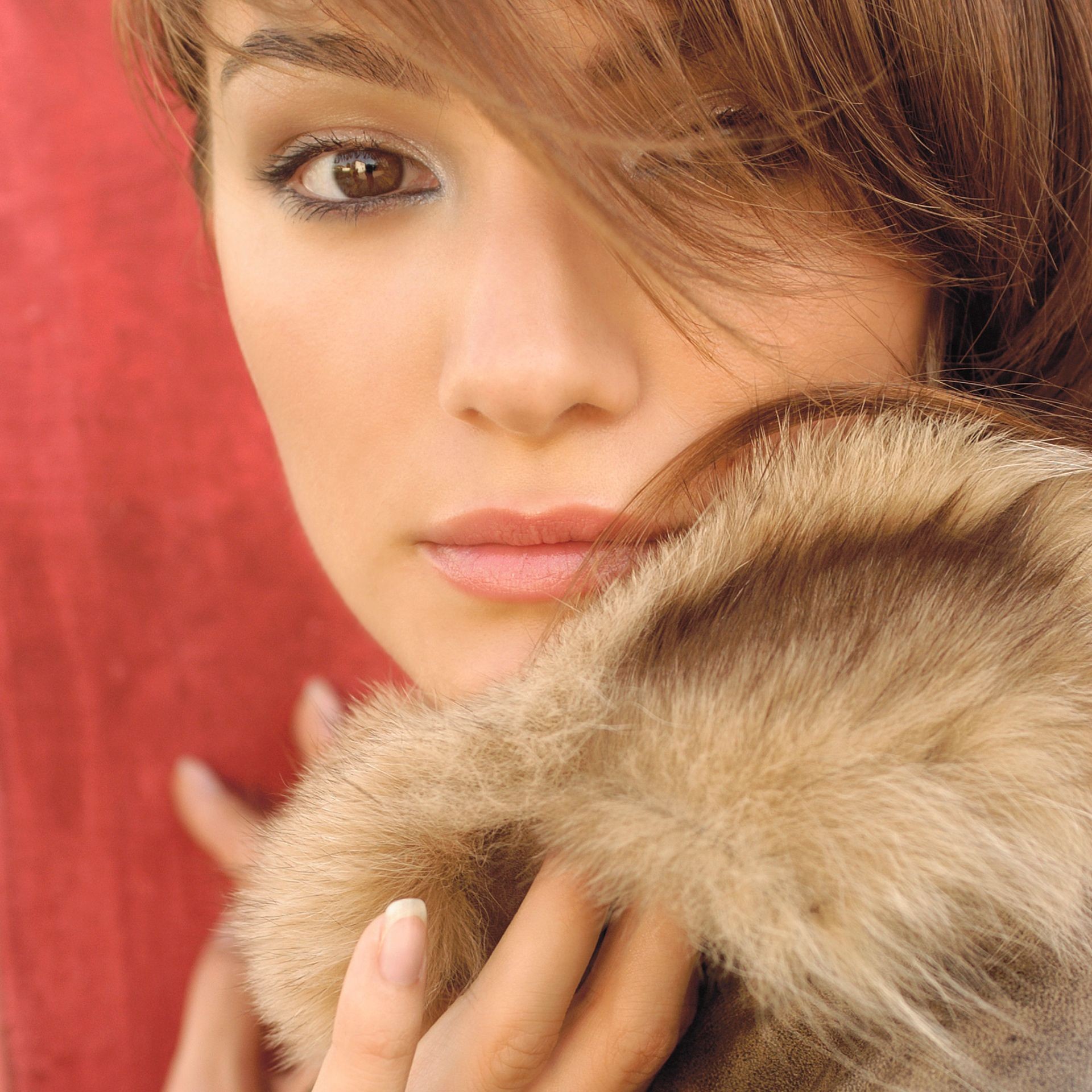 Hand with manicured nails holding the fur collar of a coat against a red background.