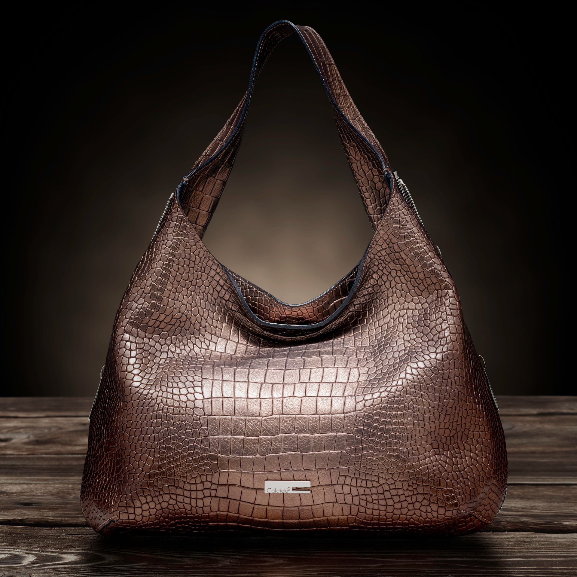 Luxury brown leather handbag with a textured crocodile pattern on a wooden surface, dramatic lighting.