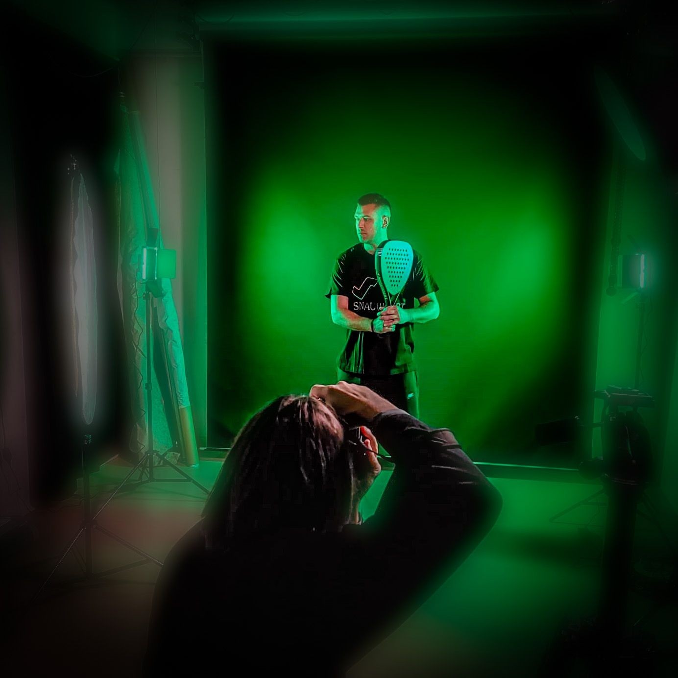 Photographer taking a photo of a person holding a paddle racket in a studio with green lighting.